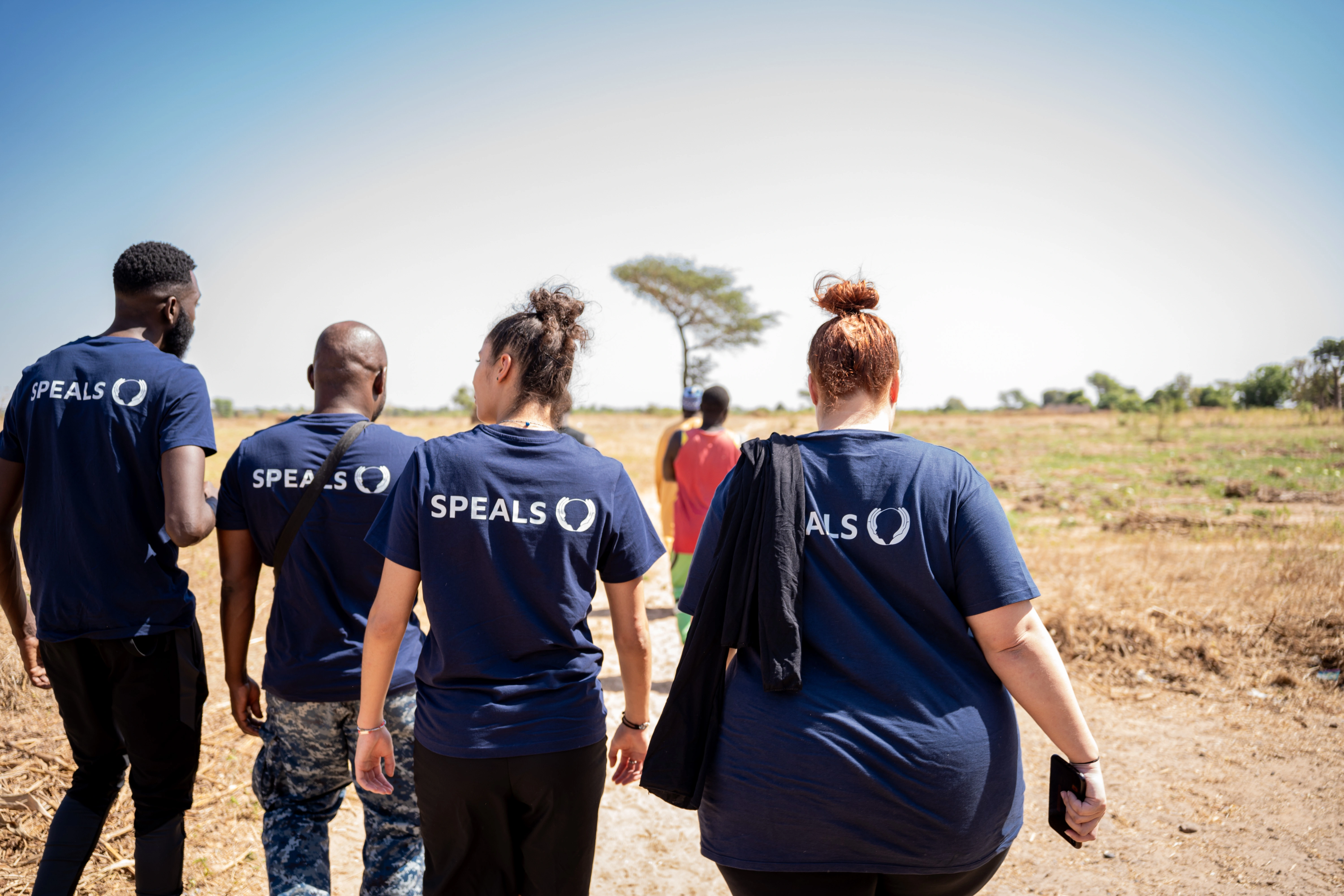 Un groupe de bénévoles portant des t-shirts speals marche sur un terrain aride en Afrique