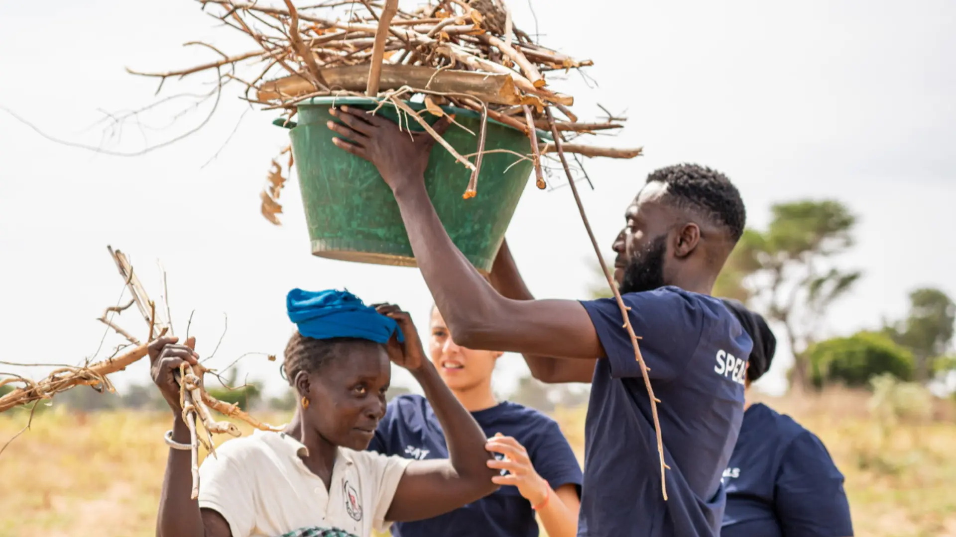 un homme aide une femme à porter un panier vert rempli de branches sur sa tete en afrique